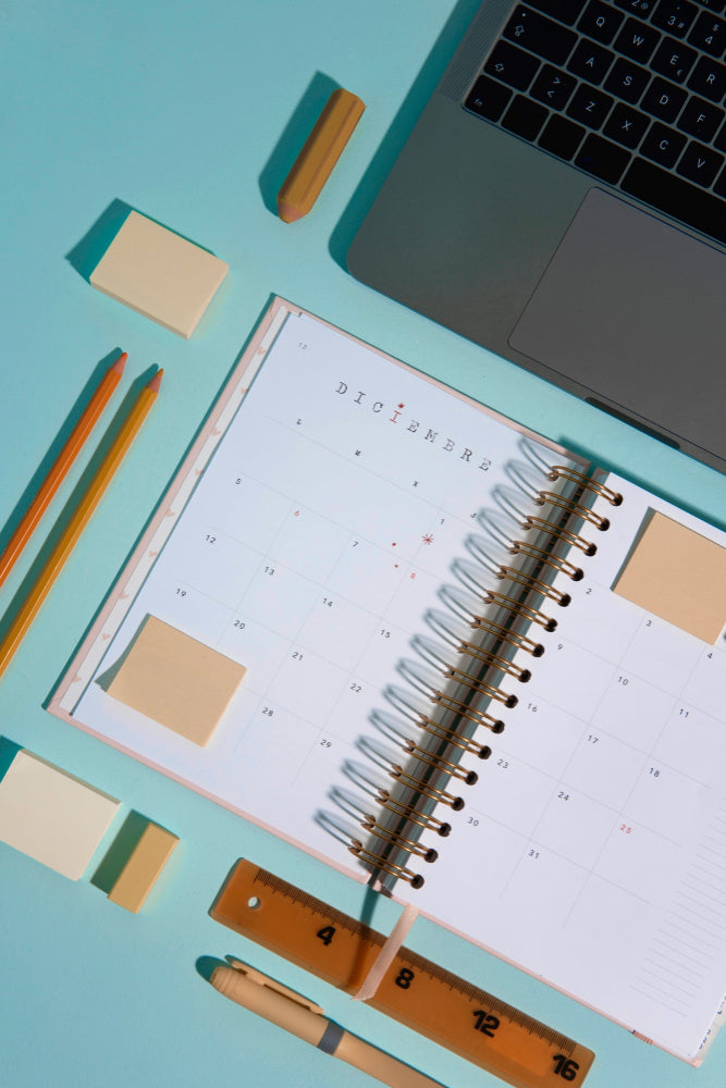 a light blue desk background with pencils, erasers, planners, and a macbook air laptop that is being used as a product category image for digital planners and organizers